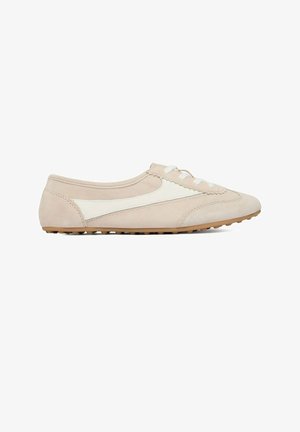 Zapatilla deportiva de ante beige con franja lateral blanca, cordones blancos y suela marrón texturizada, mostrada de perfil derecho sobre fondo blanco.