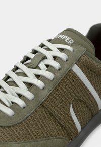 Grüner Sneaker aus Wildleder und gewebtem Textil mit weißen Schnürsenkeln, der eine strukturierte Oberfläche und einen hellgrauen Akzentstreifen aufweist. Markenname auf der Zunge.