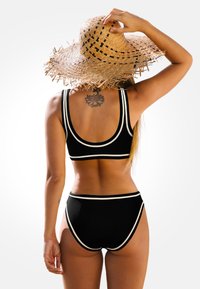 Czarny dwuczęściowy kostium kąpielowy z białymi wykończeniami, z topem na ramiączkach i wysokim stanem. W komplecie z szerokim kapeluszem słomkowym.