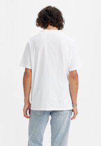 T-shirt en coton blanc à manches courtes, col rond et coupe décontractée, associé à un jean en denim bleu clair. Aucun motif visible.