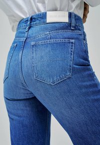 Jeans de denim azul con un diseño ajustado, que cuentan con una cintura alta, dos bolsillos traseros y una etiqueta de cuero blanco con marca en la cinturilla.
