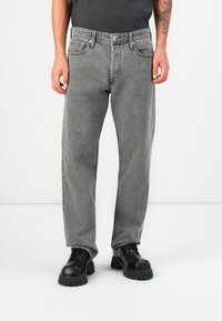 Moške sivo denim kavbojke, ravna kroja, srednje višine, pet žepov, teksturiran zaključek, v kombinaciji s črnimi debelimi vezalkami.