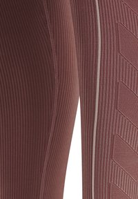 Zbliżenie na prążkowaną, mauve (fioletowo-różową) tkaninę z pionowym szwem i teksturowanym wzorem w jodełkę na sportowych legginsach.