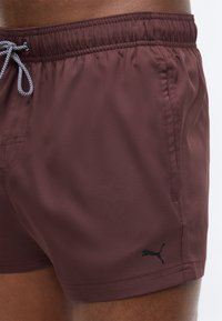 Καφέ ανδρικό μαγιό βερμούδα με μαύρο λογότυπο Puma στο αριστερό πόδι και μαύρο-άσπρο κορδόνι στη ελαστική μέση.