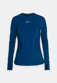 Długi rękaw sportowego topu w kolorze ciemnoniebieskim z teksturowanymi panelami bocznymi, okrągłym dekoltem i otworami na kciuki. Na piersi znajduje się logo Nike.