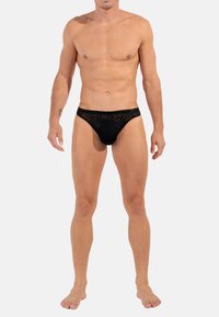 Schwarzer Spitzen-Männertanga mit transparentem Design, elastischem Bund und minimaler Bedeckung, mit floralen Mustern und einer glatten Textur.