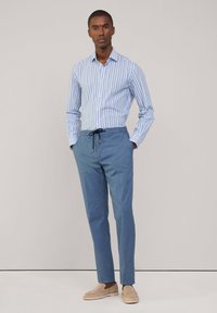 Blaue und weiße gestreifte Button-Down-Hemd, hellblaue Jogginghose mit Kordelzug und beige Slipper. Einfaches Design; glatter Stoffeindruck.