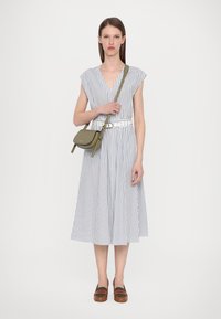Abito a righe con maniche a cap, scollatura a V profonda, vita arricciata e gonna a trapezio. Cintura bianca e borsa a tracolla verde oliva. Scarpe marroni senza chiusura.