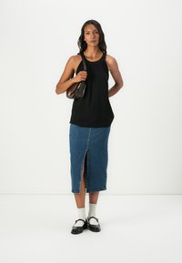 Svart ermeløs topp med plisserte detaljer i halsen, sammen med et midt-langt denimskjørt med en frontsplitt. Svarte sko med hvite sokker.