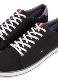 Baskets noires décontractées avec des lacets blancs, des accents gris au talon et de petits détails de drapeau rouge, blanc et bleu sur la languette et le côté.