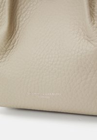 Beige színű bőr kézitáska texturált felülettel, diszkrét ezüst színű logóval, amely be van nyomva. Puha, összecsukható kialakítás, jellegzetes fémalkatrészek nélkül.