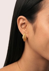 Boucles d'oreilles en métal doré en forme de clou avec un design texturé en forme de feuille. Surface brillante, forme angulaire et détails visibles rehaussent l'attrait visuel.