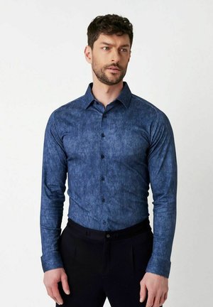 Jeanshemd im Dunkelblau mit Knöpfen, vertikalen Streifen, langen Ärmeln und klassischem Kragen. Kombiniert mit dunklen Hosen.