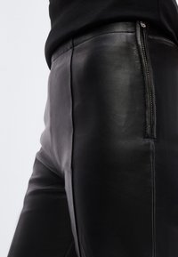 Μαύρο δερμάτινο παντελόνι με λεία υφή, διαθέτει πλευρικό φερμουάρ για κλείσιμο και εφαρμοστή γραμμή, παρουσιάζοντας έναν κομψό, μ οντέρνο σχεδιασμό.