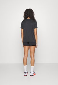 Camiseta deportiva negra de manga corta combinada con pantalones cortos negros. Presenta un ajuste holgado y una textura suave. Se lleva con calcetas blancas y zapatillas coloridas.