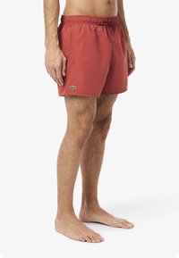 Pantaloni da nuoto rossi realizzati in materiale leggero, dotati di una vita elasticizzata, lacci, tasche laterali e un accento di logo verde sulla gamba.
