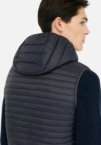 Veste matelassée marine avec un design matelassé et une capuche, dotée d'une texture douce et de manches en tricot côtelé, conçue pour la chaleur et le confort.