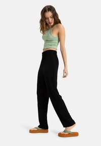 Top a coste verde chiaro, pantaloni a gamba larga neri e sandali platform marroni con cinturini verdi, caratterizzati da una vestibilità rilassata e una consistenza morbida.