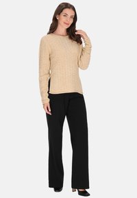 Beige kötött pulóver, texturált mintával, kerek nyakkal és hosszú ujjakkal, fekete nadrággal és magassarkú cipővel párosítva.