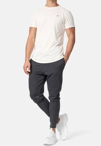 Witte katoenen T-shirt met korte mouwen en klein logo, gecombineerd met donkergrijze joggingsbroek en witte sportschoenen.