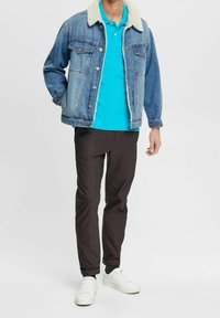 Veste en denim avec col en fausse fourrure, chemise bleu clair, pantalon noir et baskets blanches, présentant une tenue décontractée à plusieurs couches.