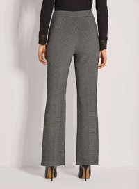 Vrouw in hoge taille, met zwart-wit geometrisch patroon op haar broek en zwarte hoge hakken, gezien van achteren.