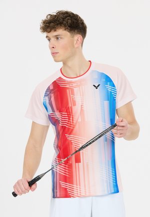 Ung mand holder en badmintonketcher iført en rød, hvid og blå mønstret sportstrøje og hvide shorts, ser til siden.