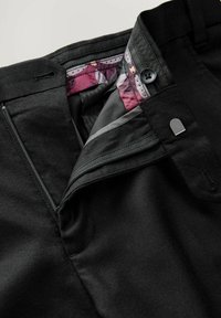 Pantalons noirs avec fermeture éclair, bouton de fermeture, et doublure intérieure de la ceinture à motifs dans des nuances de violet et de gris.