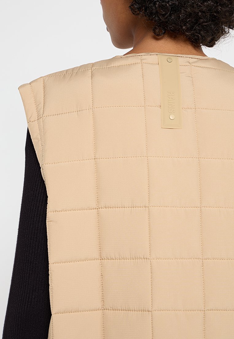 Beige ärmellose, gesteppte Weste mit glatter Textur, versehen mit einem rechteckigen Etikett auf der Rückseite mit dem Markennamen "RAINS."