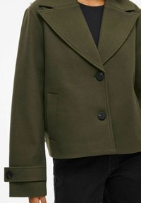 Olijfgroene wolmix jas, cropped met een brede revers, twee knopen sluiting en zijzak. Heeft een gestructureerde Silhouette en textiel stof.