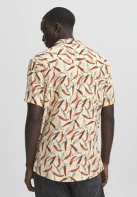 Rövid ujjú, elegáns ing krém színben, színes madár- és chili paprika mintával. Könnyű anyag, sima tapintással.