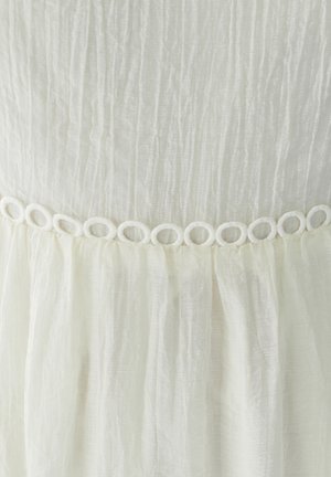 Hvid plisseret stof med en tekstureret overflade, der har en dekorativ løkket kant ved taljen. Blødt og let materiale.