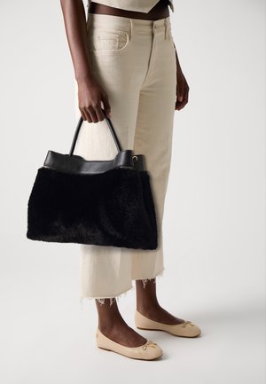 Persoon die gebroken witte cropped jeans en beige ballerina's draagt, met een grote zwarte handtas van nepbont met leren handvatten.