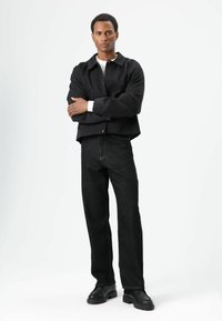 Black cropped jacket over a white shirt, paired with dark jeans and black boots. The outfit features a simple design and tailored fit.