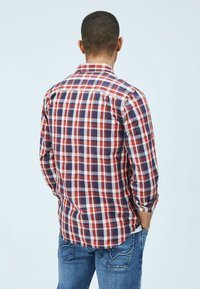 Rot-weiße-und-blaue Karoshemd mit langen Ärmeln, Button-Down-Kragen und einem leicht geschwungenen Saum, getragen mit blauen Jeans.