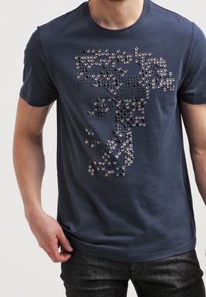 T-shirt en coton bleu marine avec un motif en relief composé de clous métalliques carrés formant un dessin graphique à l'avant. Manches courtes.