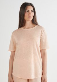 Ljus persikofärgad t-shirt med kort ärm och rund halsringning, tillverkad av mjukt, lätt tyg, med en subtil textur och avslappnad passform.