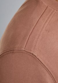 Katoenen top in een gedempte rozenkleur, met een ronde halslijn, gestructureerd oppervlak en schoudernaden met nette stiksels en subtiele accenten.