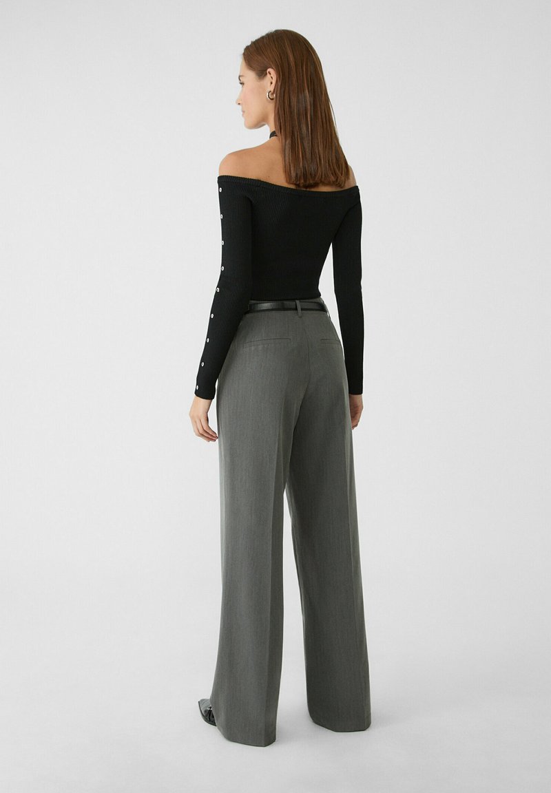 Haut noir à épaules dénudées en tissu côtelé avec des manches longues et des accents de boutons argentés, associé à un pantalon gris à taille haute et à jambe large.