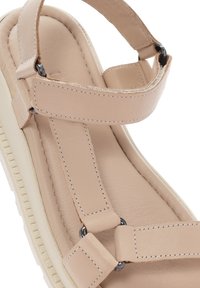 Sandale en cuir beige avec de larges brides, dotée de quincailleries en métal et d'une semelle intérieure rembourrée. Le design offre un look moderne et minimal.