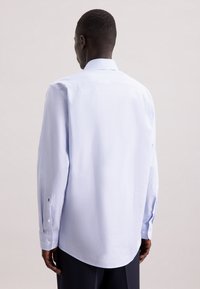 Camicia azzurra a maniche lunghe realizzata in tessuto testurizzato, con colletto a bottoni e polsini abbottonati. La vista posteriore mostra un orlo arrotondato.