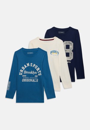 Trois t-shirts à manches longues col rond en bleu, crème et marine avec des textes et chiffres sur le thème du sport à l'avant et sur la manche.