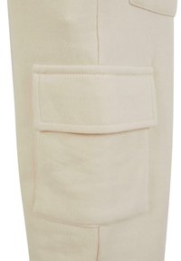 Pantalons cargo en coton beige avec une grande poche carrée sur la cuisse, présentant des bords cousus et une finition douce et texturée.
