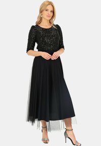 Długa czarna sukienka z cekinowym gorsetem, krótkimi bufkami i zwiewną spódnicą z tiulu. Połączona z srebrnymi butami na obcasie ozdobionymi błyskotkami.