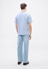 Világoskék, rövid ujjú pamut póló, amely laza világos farmernadrággal van párosítva. A ruházat laza sziluettet mutat.