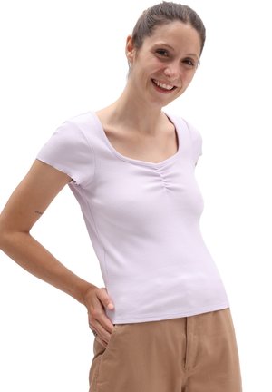 T-shirt lilla a coste con maniche corte, scollatura quadrata e dettaglio arricciato sul petto, abbinata a pantaloni beige.