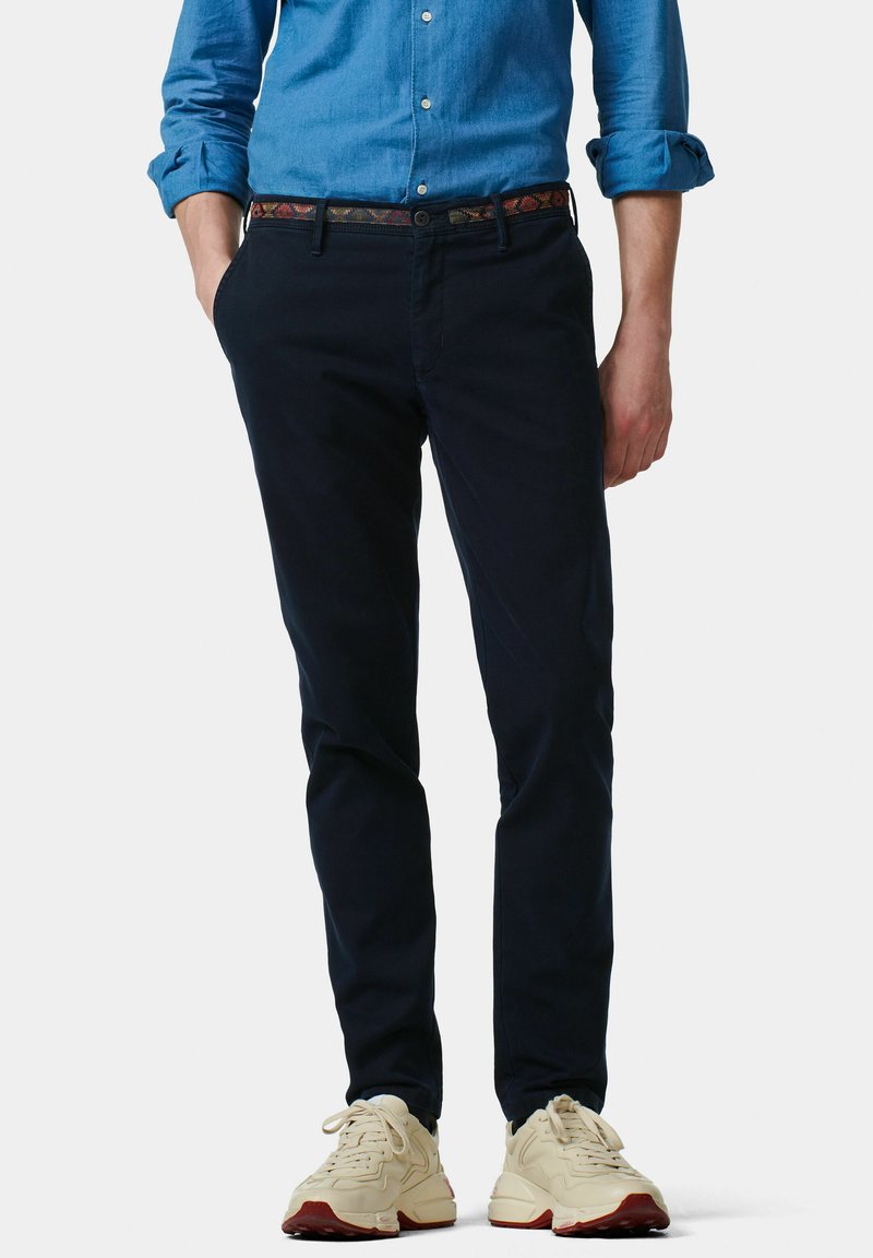Marineblauwe chinos met een slim fit, gemaakt van zachte katoen. Gecombineerd met een geborduurde riem en crèmekleurige sneakers met rode accenten.
