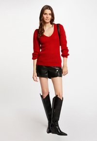 Maglione rosso a maglia con scollo a V, maniche lunghe a sbuffo, abbinato a pantaloni di pelle neri e stivali neri con punta a ginocchio.