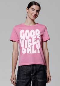 Roze katoenen t-shirt met een opvallende witte grafische tekst "GOOD VIBES ONLY" op de voorkant. Korte mouwen en een ronde hals.