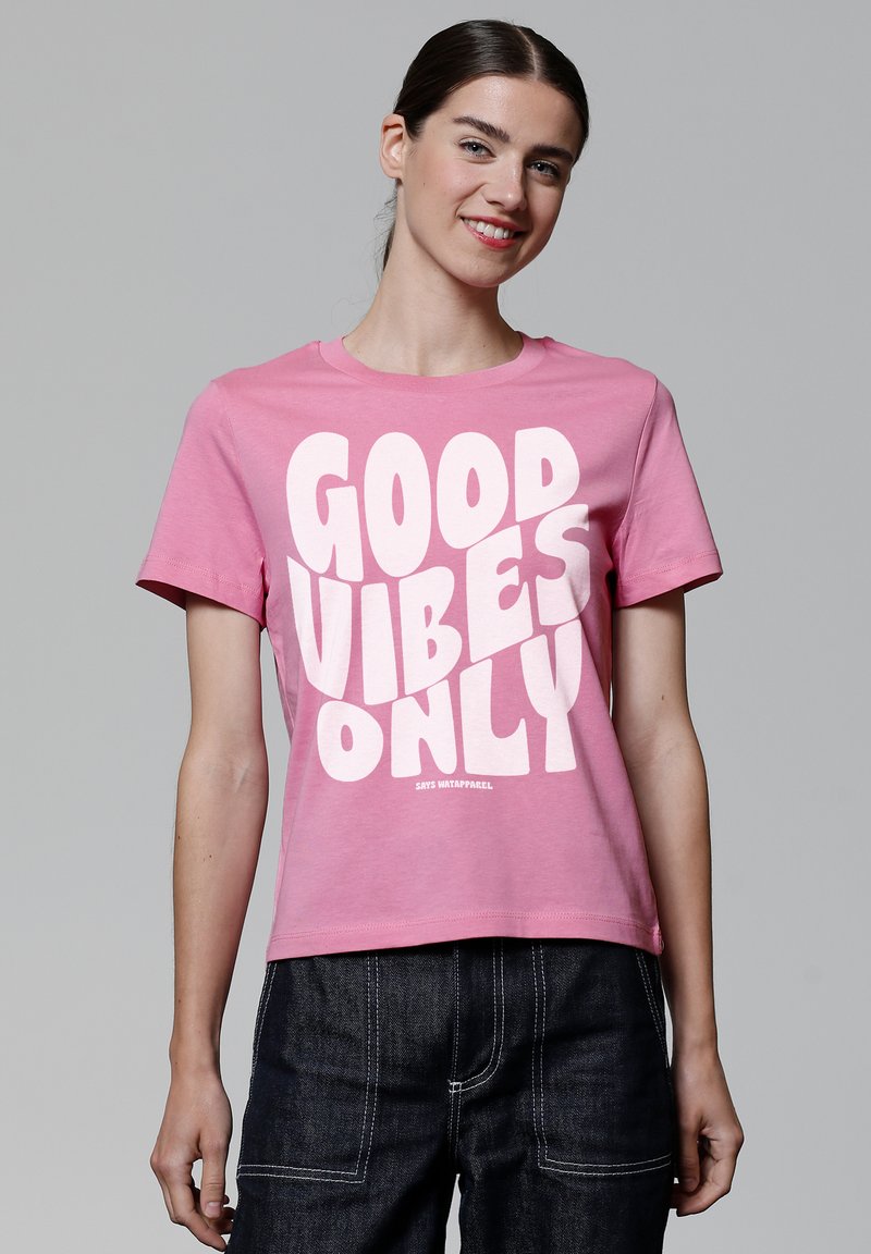 Roze katoenen t-shirt met een opvallende witte grafische tekst "GOOD VIBES ONLY" op de voorkant. Korte mouwen en een ronde hals.